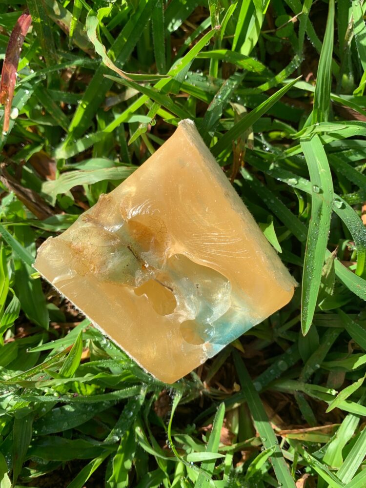 Resin art experiment using a paper cup with embedded flower petals and mica pigments in gold and blue, displayed on grass.